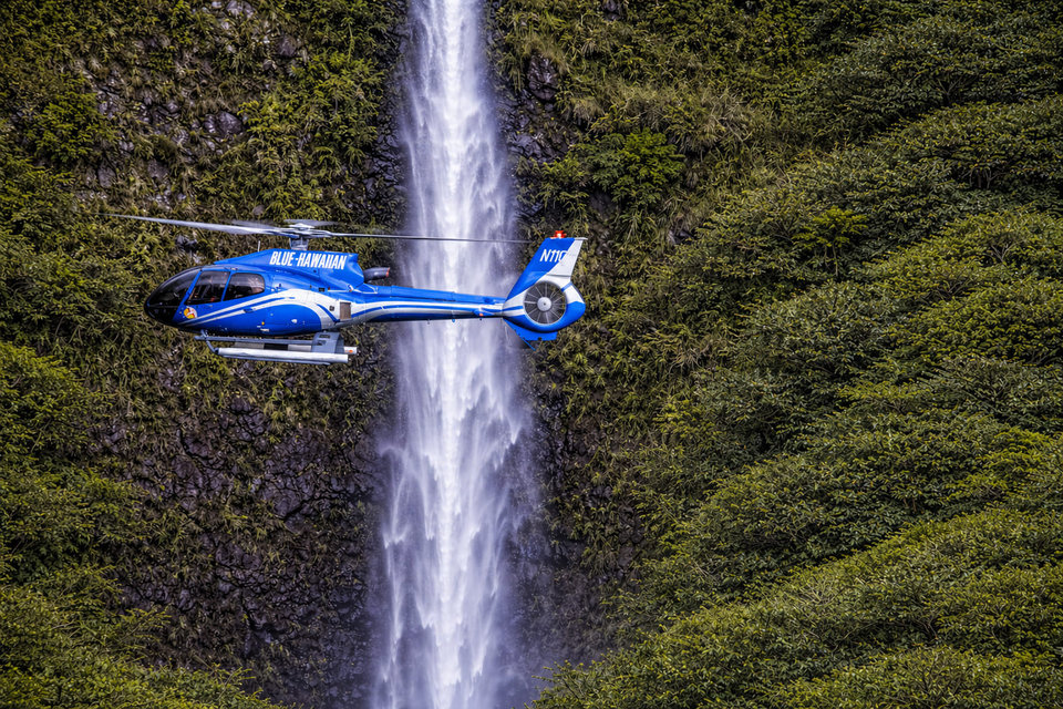 A helicopter flying beside a Kauai waterfall